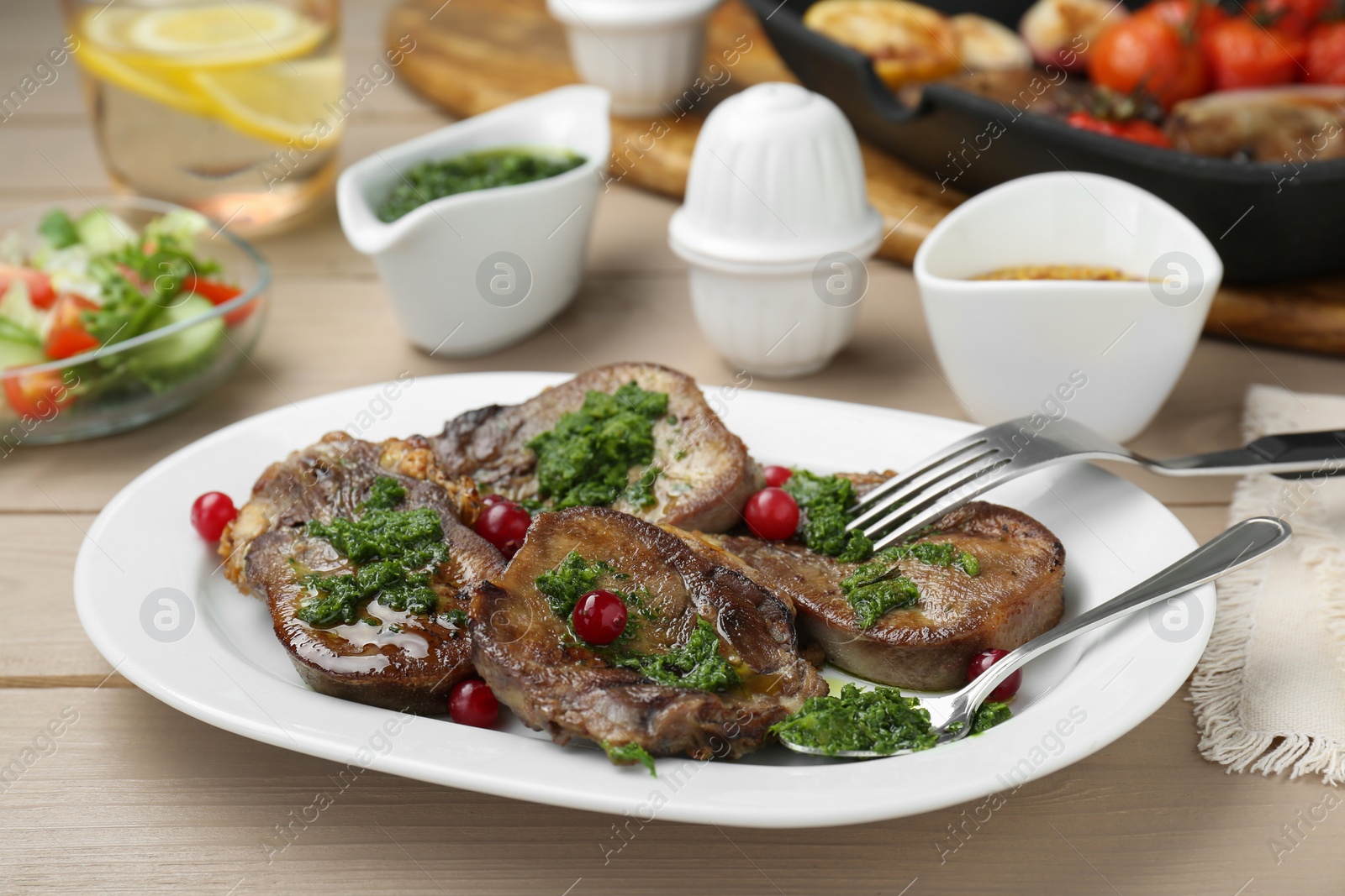Photo of Tasty beef tongue pieces, salsa verde and berries on beige wooden table, closeup