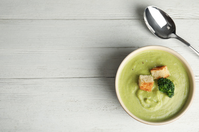 Photo of Delicious broccoli cream soup with croutons served on white wooden table, flat lay. Space for text