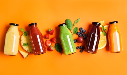 Flat lay composition with bottles of delicious juices and fresh ingredients on orange background