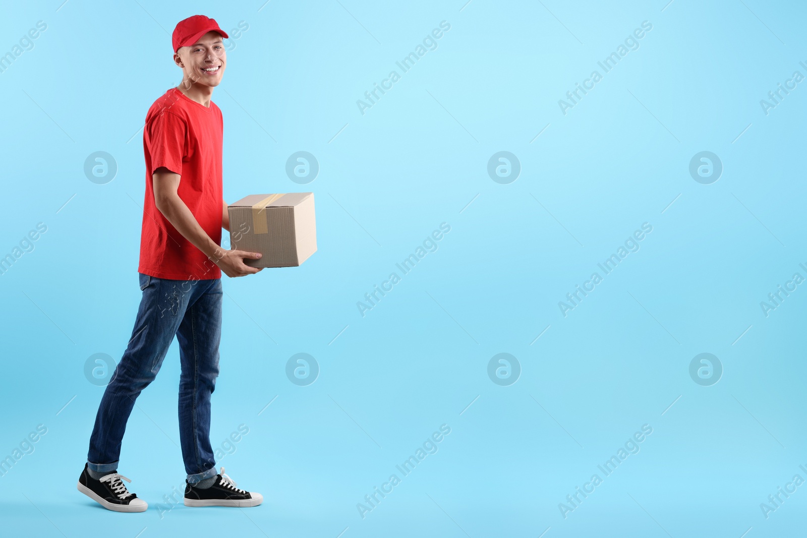 Photo of Happy courier with parcel on light blue background. Space for text