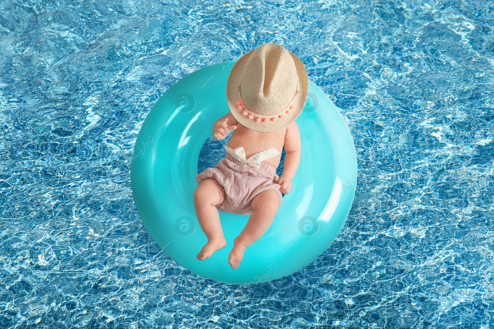 Image of Cute little baby with inflatable ring in swimming pool, top view