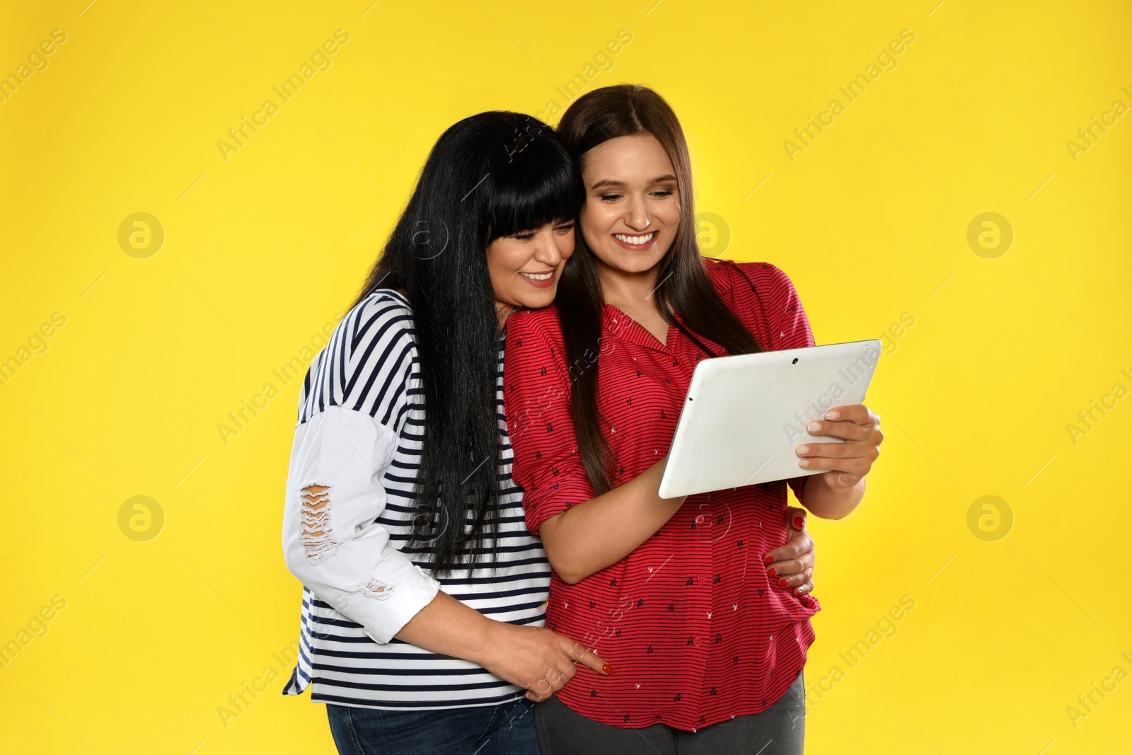 Photo of Young daughter and her mature mother with tablet computer on color background