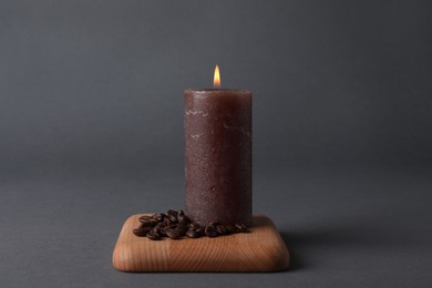 Burning candle with coffee beans on grey background