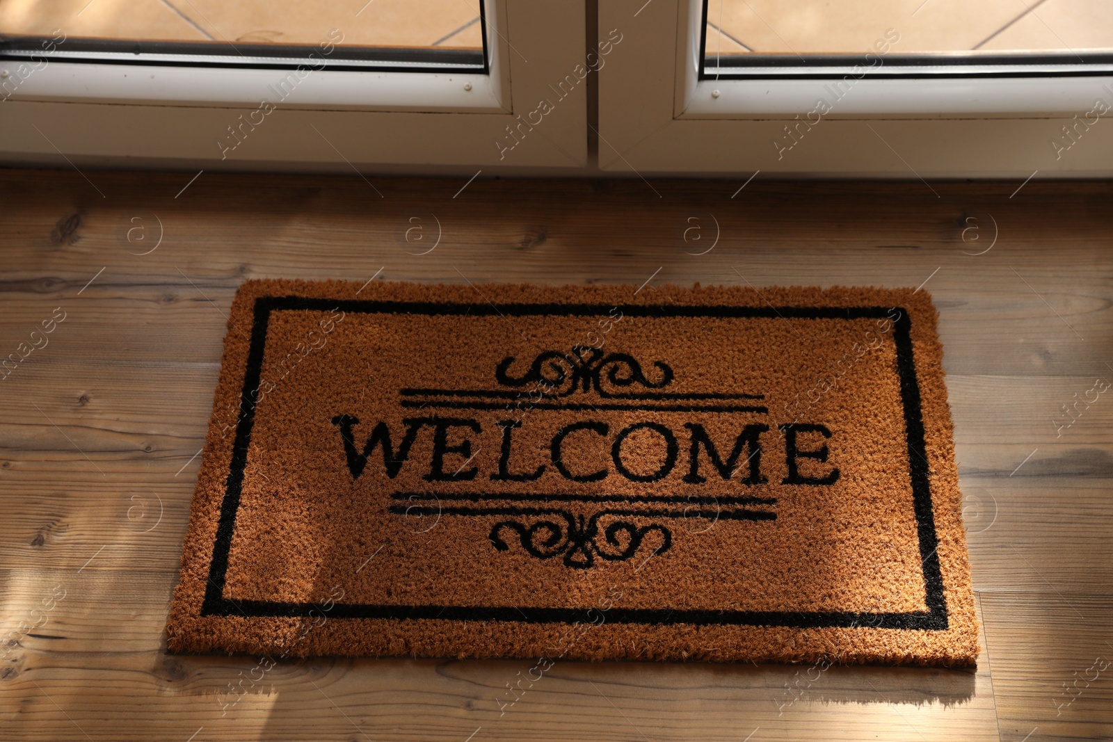 Photo of Door mat with word Welcome on wooden floor near entrance