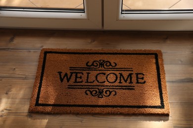 Photo of Door mat with word Welcome on wooden floor near entrance