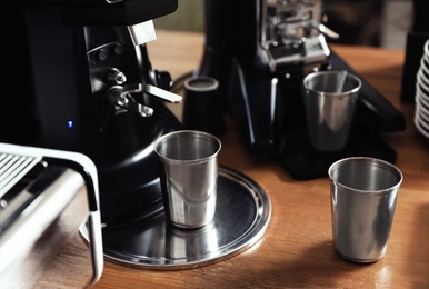 Photo of Metal cups near coffee grinding machine on wooden table
