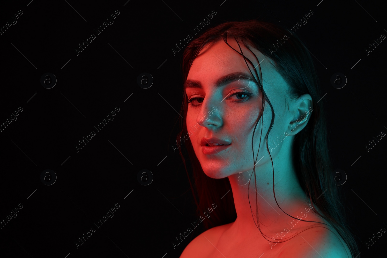 Photo of Portrait of beautiful woman in neon lights against black background. Space for text