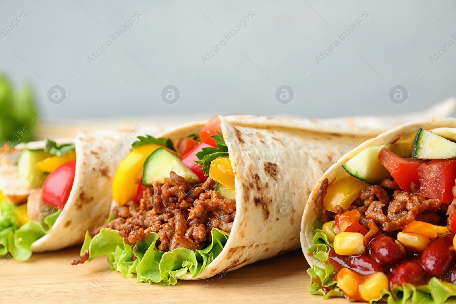 Photo of Board with delicious meat tortilla wraps on grey background, closeup