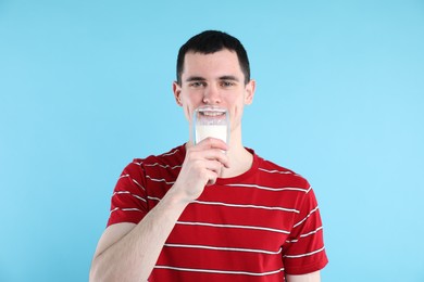 Milk mustache left after dairy product. Man drinking milk on light blue background