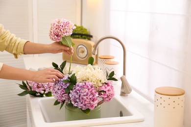 Photo of Woman making bouquet with beautiful hydrangea flowers in kitchen, closeup