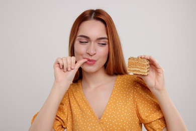 Young woman eating piece of tasty cake on light grey background