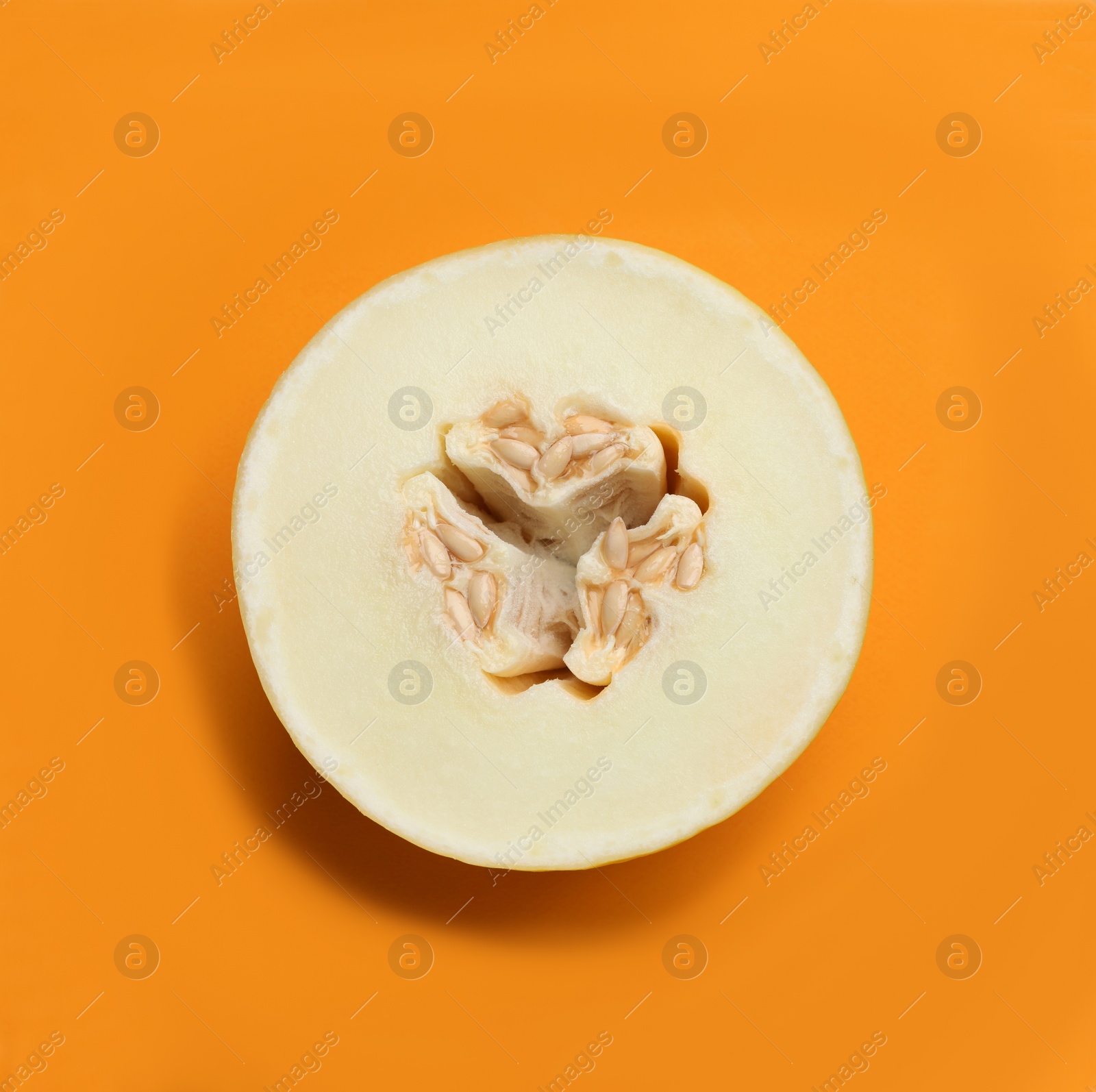 Photo of Half of ripe tasty melon on orange background, top view