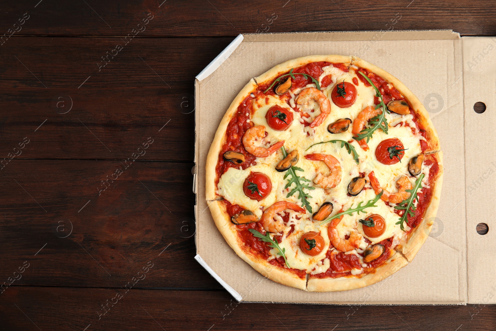 Photo of Delicious seafood pizza in cardboard on wooden table, top view. Space for text