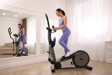 Photo of Woman using modern elliptical machine at home