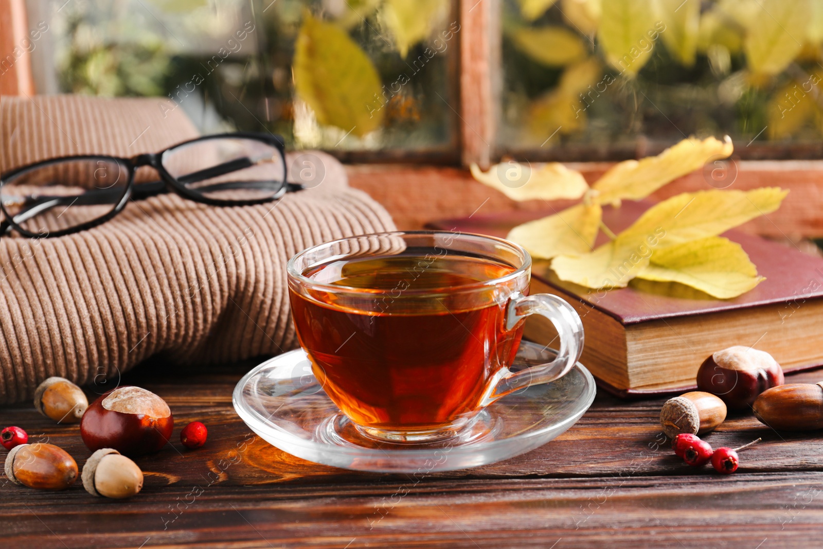 Photo of Cup of aromatic tea, book and soft sweater on wooden windowsill indoors. Autumn atmosphere