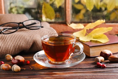 Cup of aromatic tea, book and soft sweater on wooden windowsill indoors. Autumn atmosphere