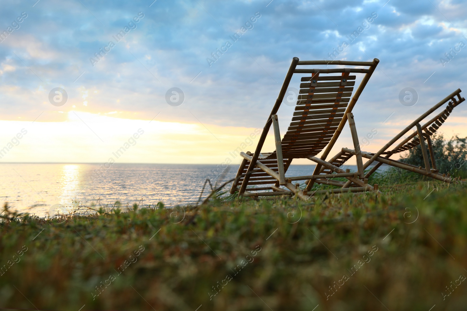 Photo of Empty wooden deckchairs on hill near calm river