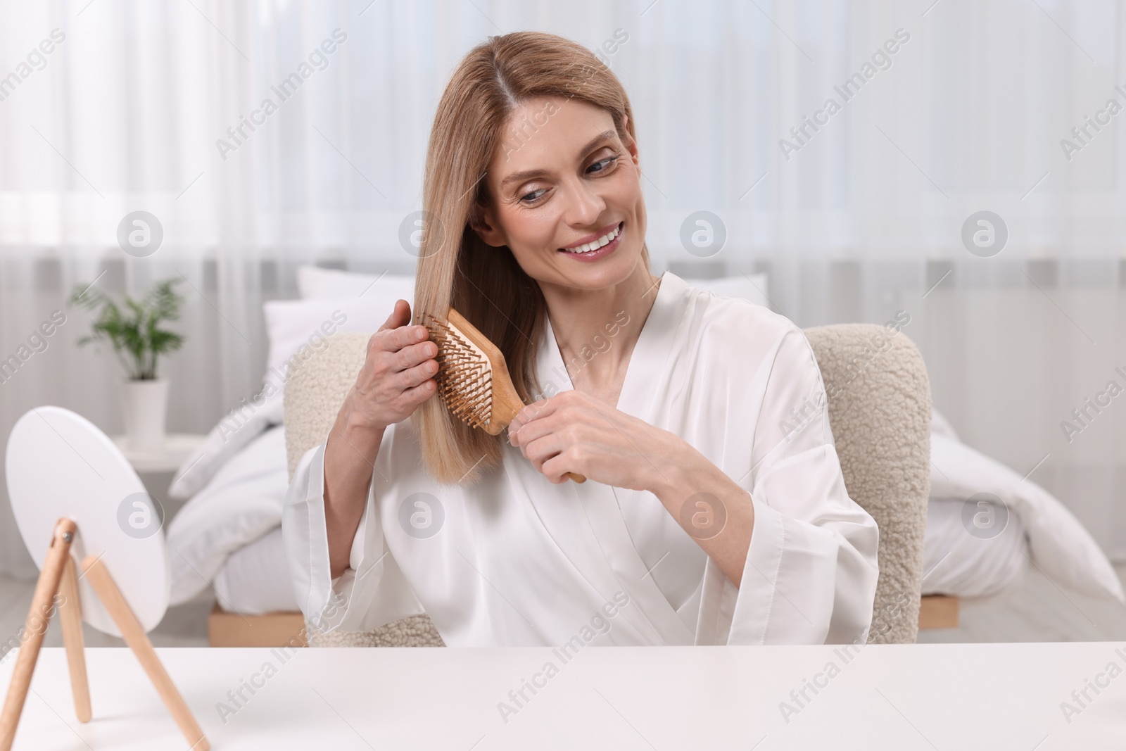 Photo of Beautiful woman brushing her hair at vanity in bedroom