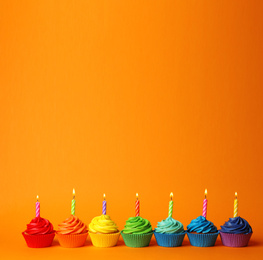 Photo of Delicious birthday cupcakes with burning candles on orange background