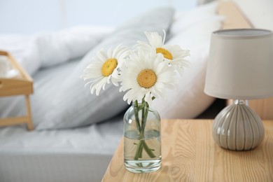 Photo of Bouquet of beautiful daisy flowers and lamp on nightstand in bedroom