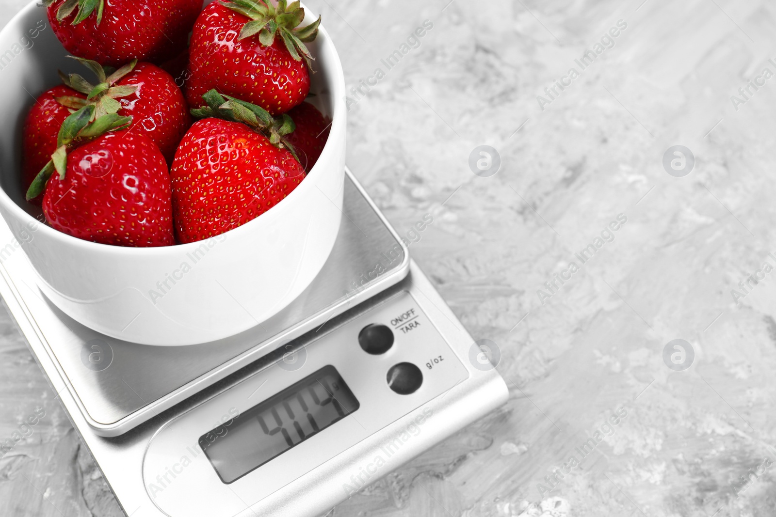 Photo of Kitchen scale with bowl of strawberries on grey textured table, closeup. Space for text