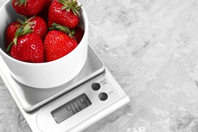 Kitchen scale with bowl of strawberries on grey textured table, closeup. Space for text