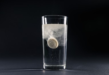 Photo of Effervescent pill dissolving in glass of water on grey table