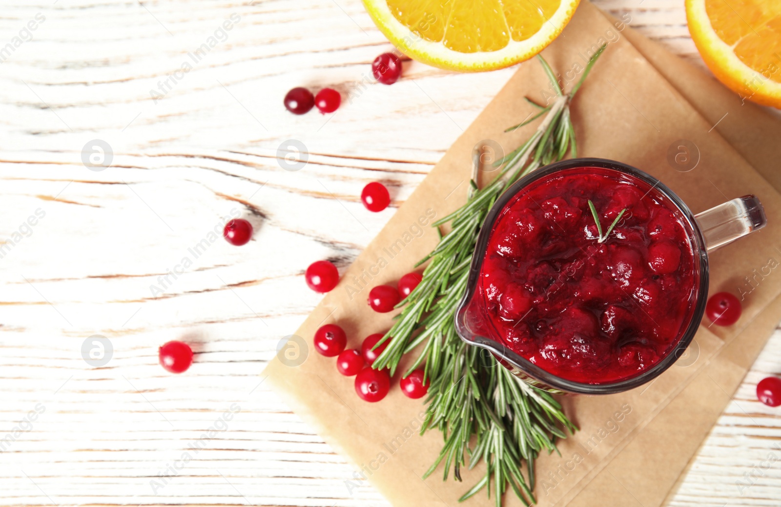 Photo of Tasty cranberry sauce in pitcher with rosemary on white wooden background, flat lay. Space for text