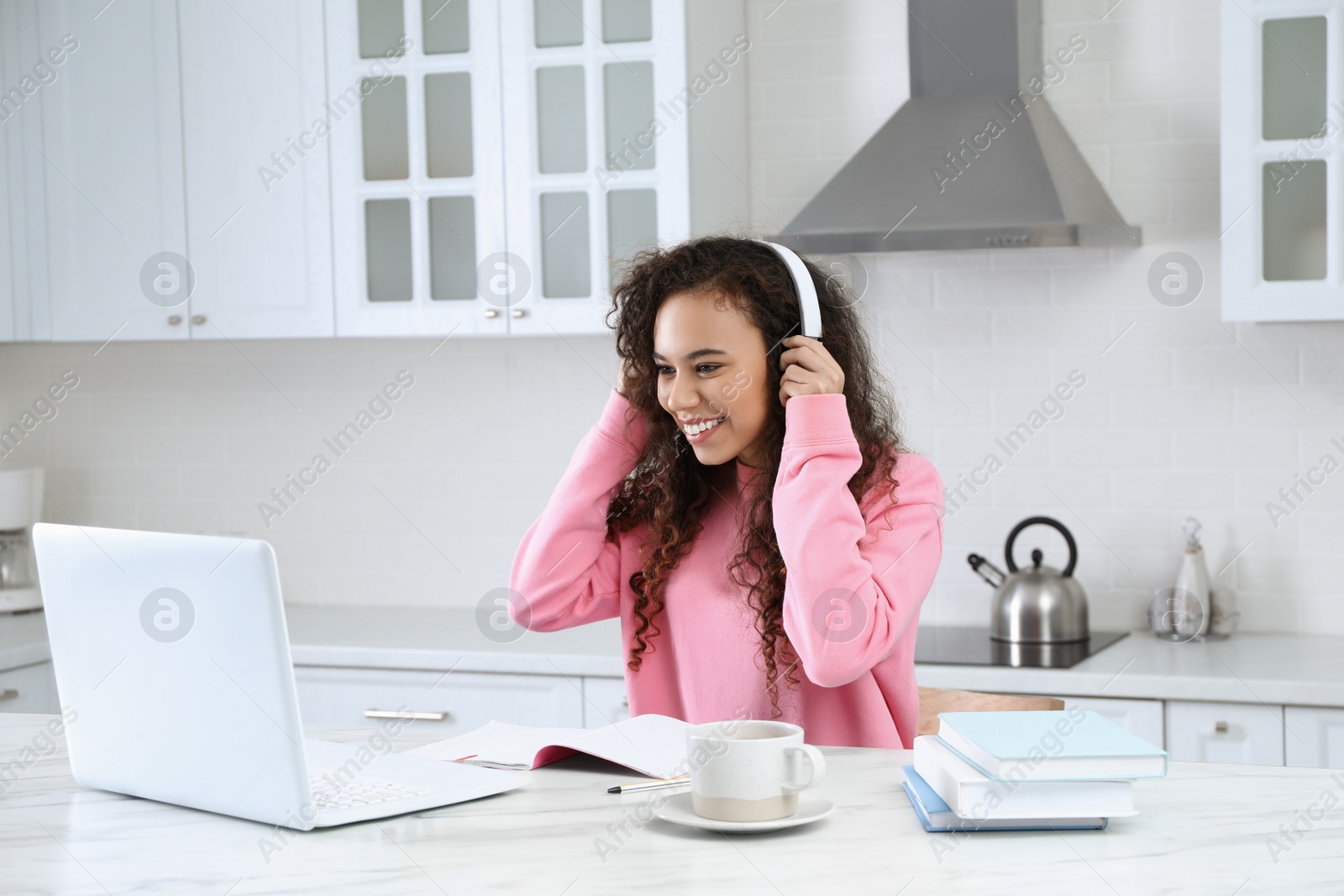 Photo of African American woman with modern laptop and headphones studying in kitchen. Distance learning