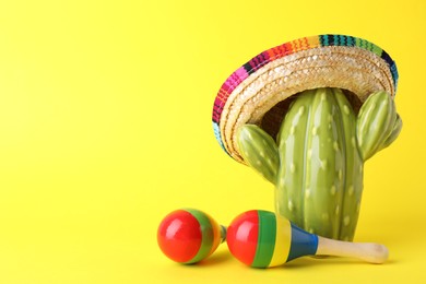 Photo of Colorful maracas and toy cactus with sombrero hat on yellow background, space for text. Musical instrument