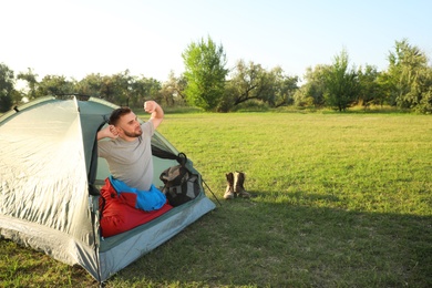 Young man in sleeping bag stretching inside camping tent