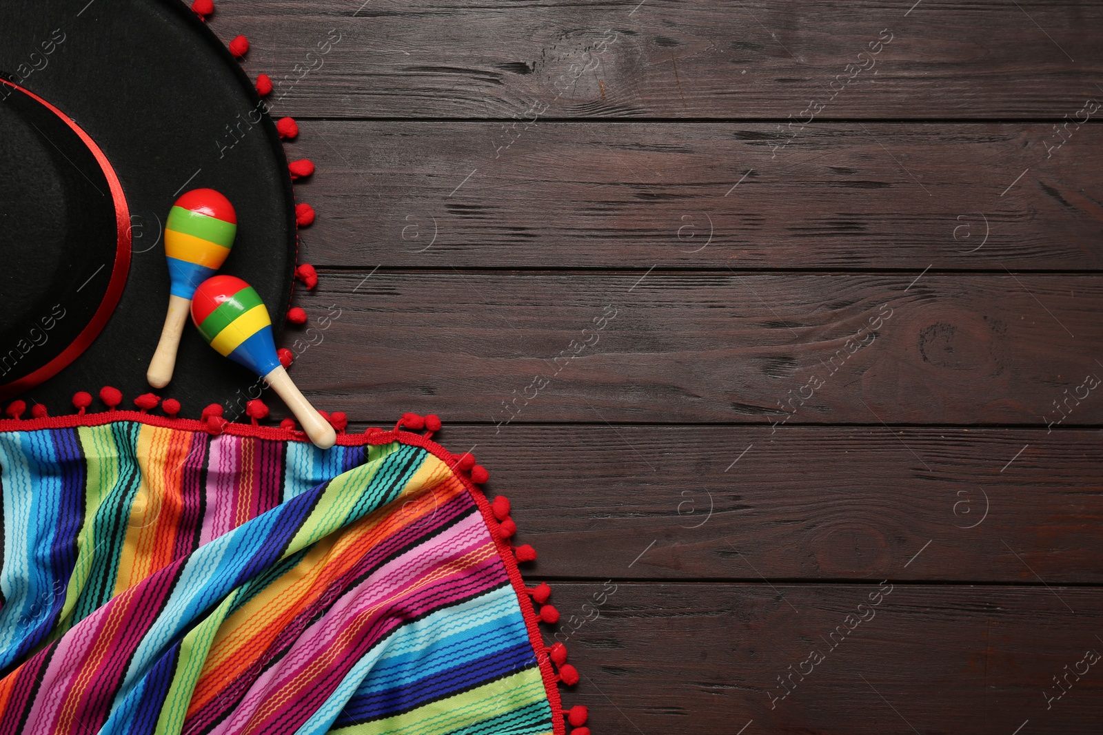 Photo of Mexican sombrero hat, maracas and colorful poncho on wooden background, flat lay. Space for text