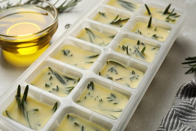 Photo of Ice cube tray with herbs frozen in oil and fresh rosemary on grey table, closeup