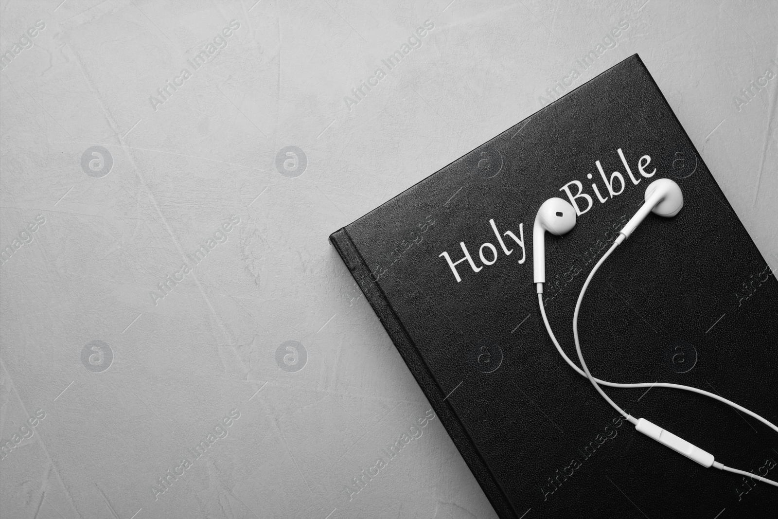 Photo of Bible and earphones on light grey background, top view with space for text. Religious audiobook