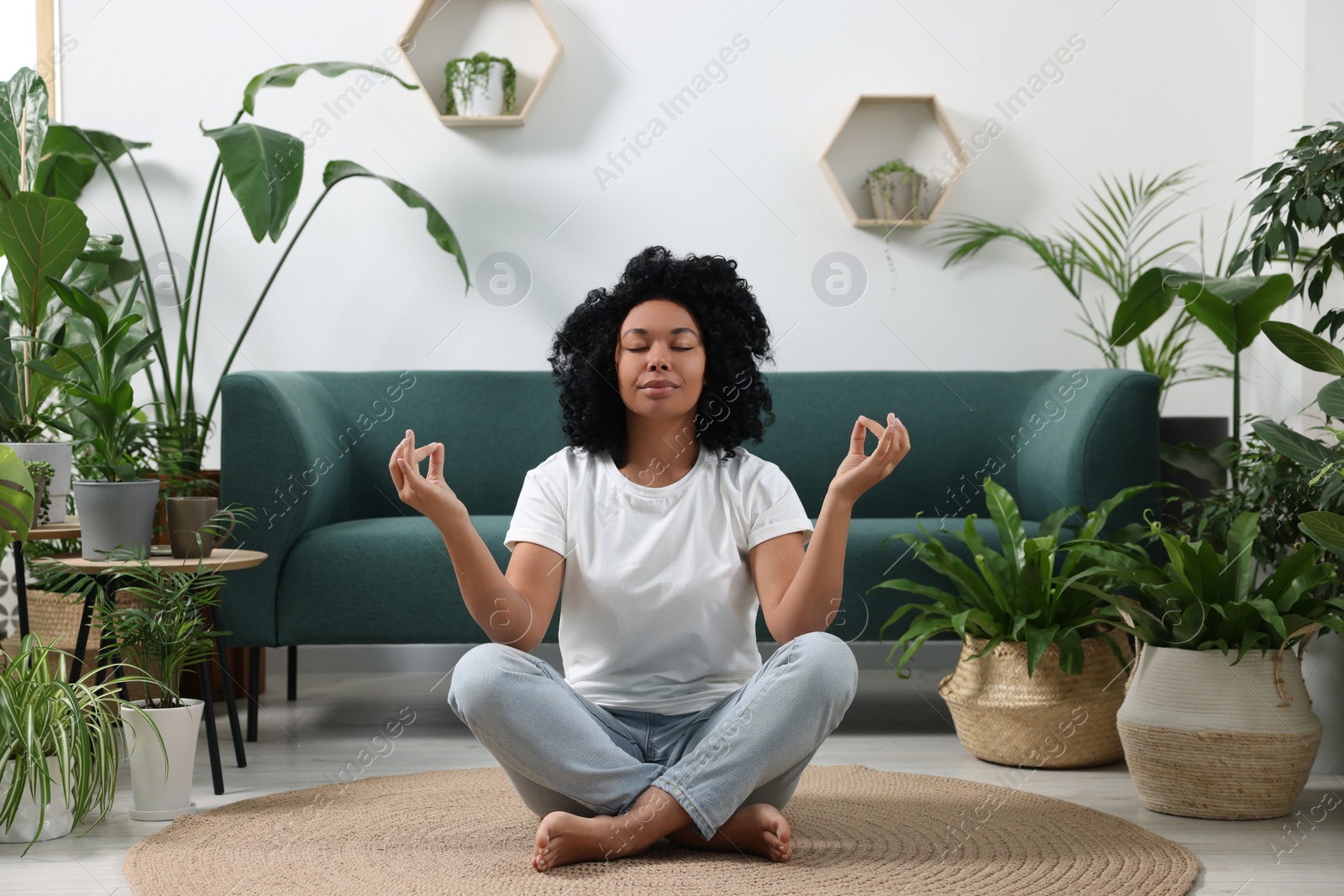 Photo of Relaxing atmosphere. Woman meditating near potted houseplants in room