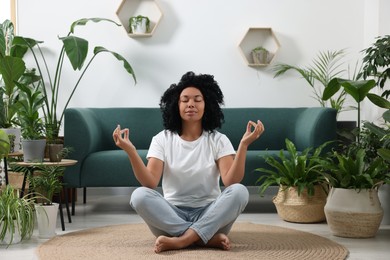 Relaxing atmosphere. Woman meditating near potted houseplants in room