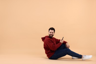 Handsome young man using smartphone on beige background, space for text