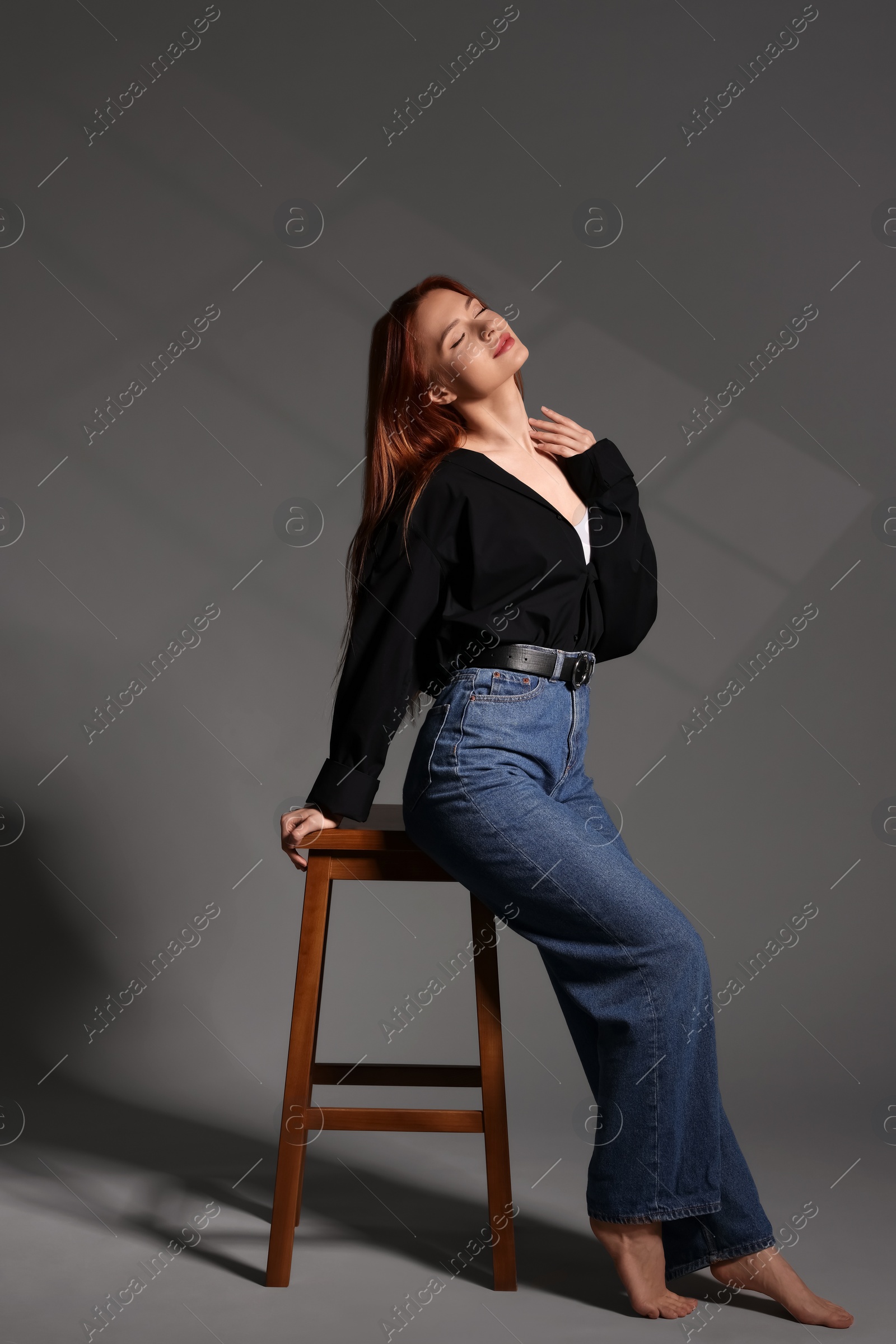 Photo of Beautiful young woman sitting on stool against gray background