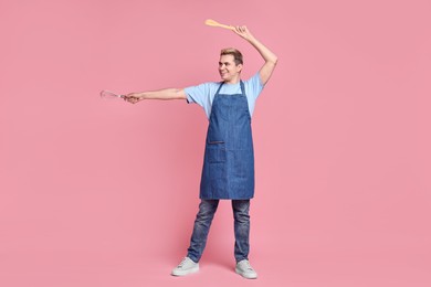 Photo of Portrait of happy confectioner holding spatula and whisk on pink background