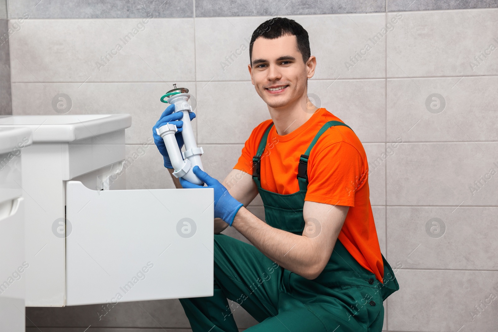 Photo of Smiling plumber wearing protective gloves repairing sink in bathroom