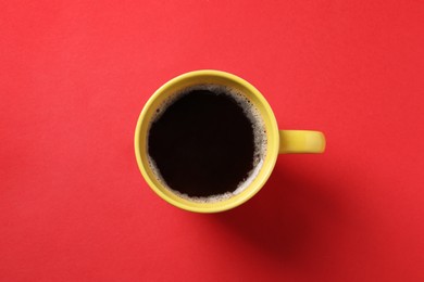 Cup of aromatic coffee on red background, top view