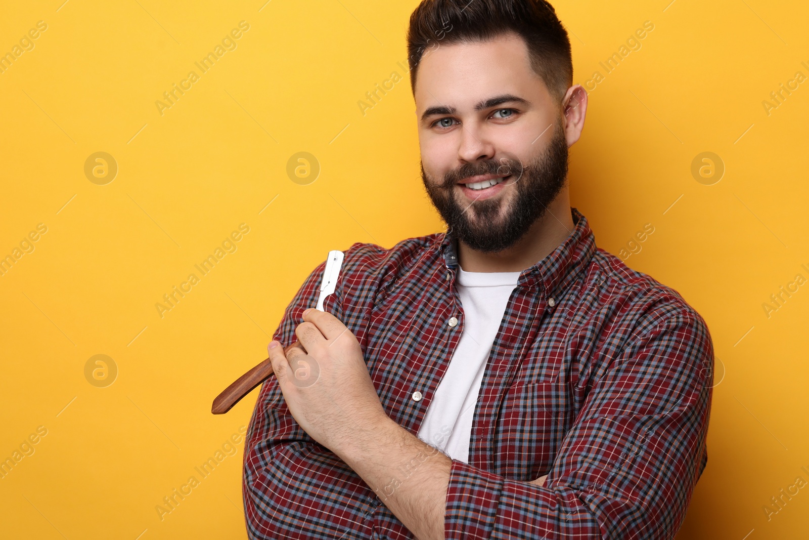 Photo of Handsome young man with mustache holding shaving blade on yellow background