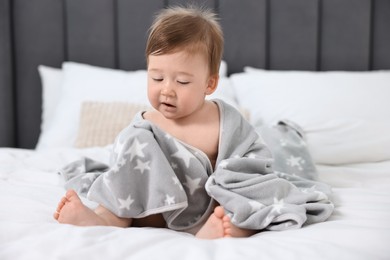 Cute baby boy with blanket sitting on bed at home