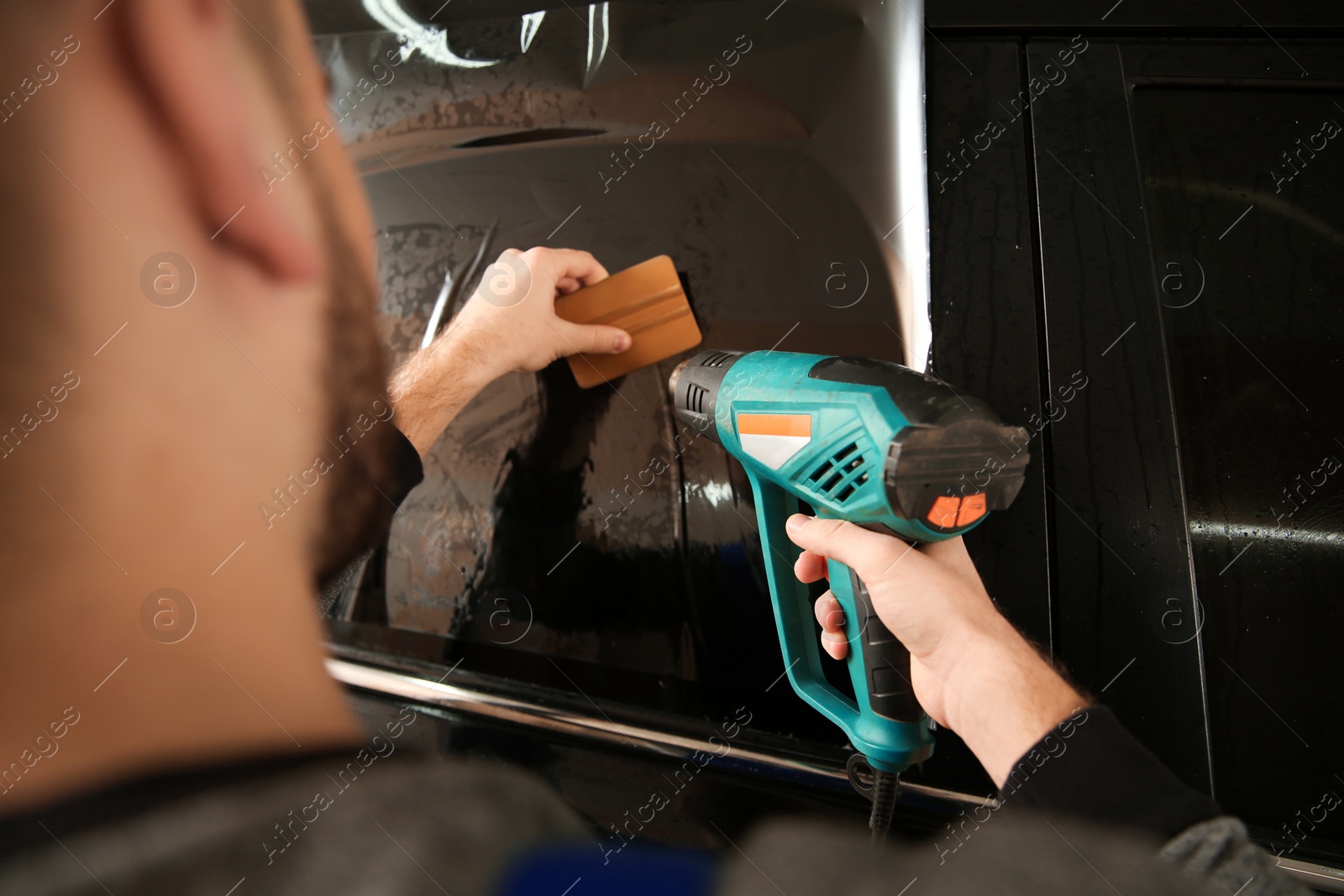 Photo of Worker tinting car window in shop, closeup