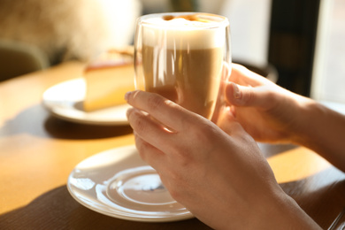 Photo of Woman with cup of delicious latte at table, closeup