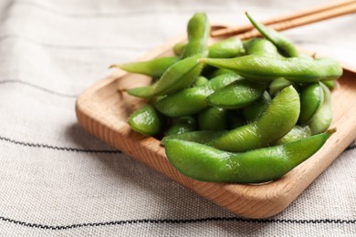 Photo of Wooden plate with green edamame beans in pods on towel, closeup