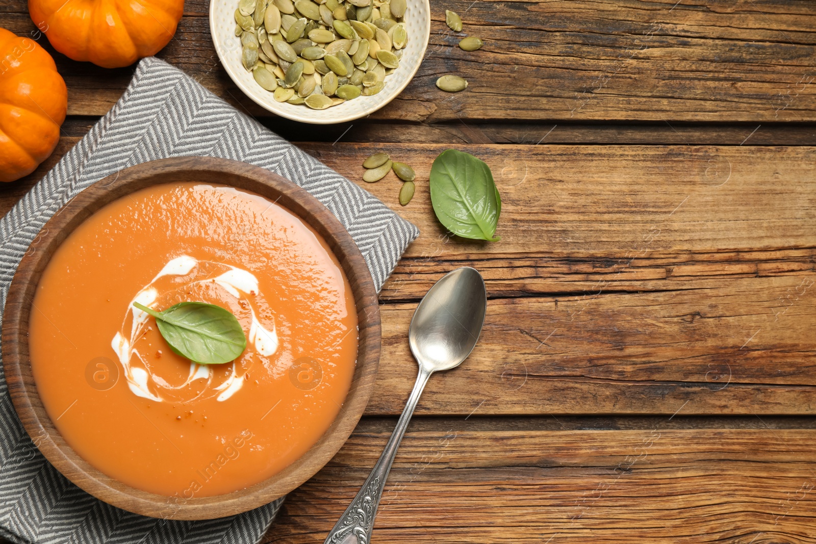 Photo of Tasty creamy pumpkin soup with basil in bowl on wooden table, flat lay. Space for text