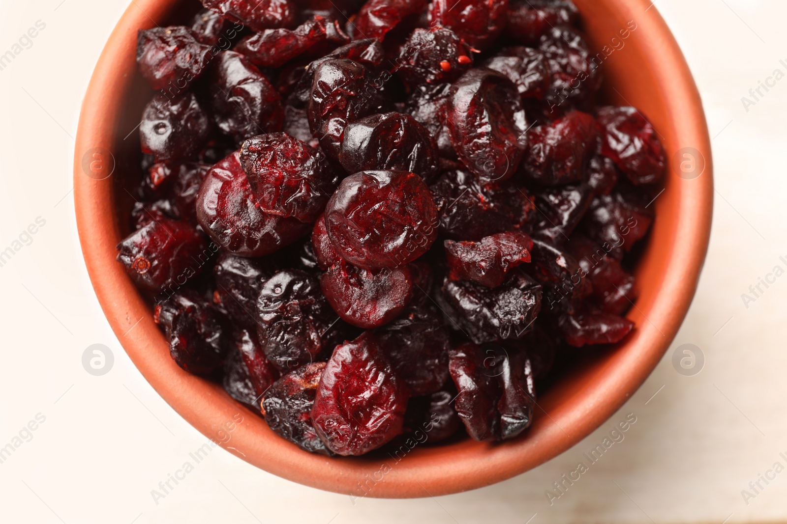Photo of Tasty dried cranberries in bowl on light table, top view