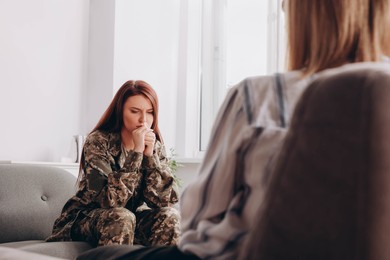 Sad female military officer sitting on sofa in psychologist office