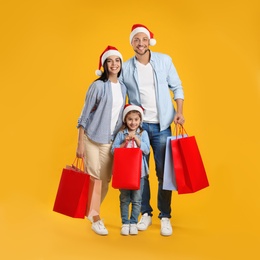 Photo of Happy family with paper bags on yellow background. Christmas shopping